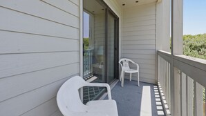 A balcony with white plastic chairs, a glass door leading to an interior room, and a wooden railing. - Dunescape 132-Ocean Front Condo w/Pool (Atlantic Beach)
