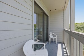 A balcony with white plastic chairs, a glass door leading to an interior room, and a wooden railing. - Dunescape 132-Ocean Front Condo w/Pool (Atlantic Beach)