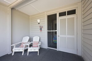 A balcony with two Adirondack chairs, a small table, and a door leading to a closet. - Dunescape 132-Ocean Front Condo w/Pool (Atlantic Beach)