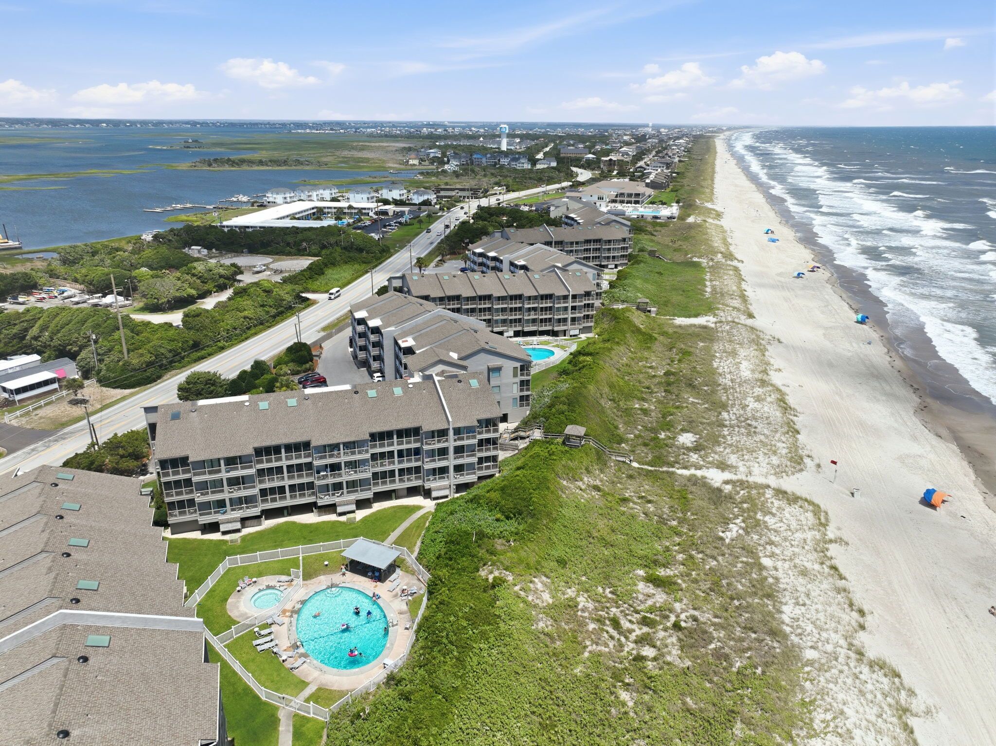 A coastal hotel with multiple buildings, a swimming pool, and a beach.