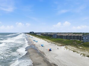 A beach with a row of buildings, some with balconies, and a clear sky. - Dunescape 132-Ocean Front Condo w/Pool (Atlantic Beach)