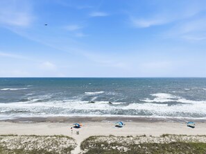 A beach with three umbrellas, a flag, and a bird in the sky. - Dunescape 132-Ocean Front Condo w/Pool (Atlantic Beach)