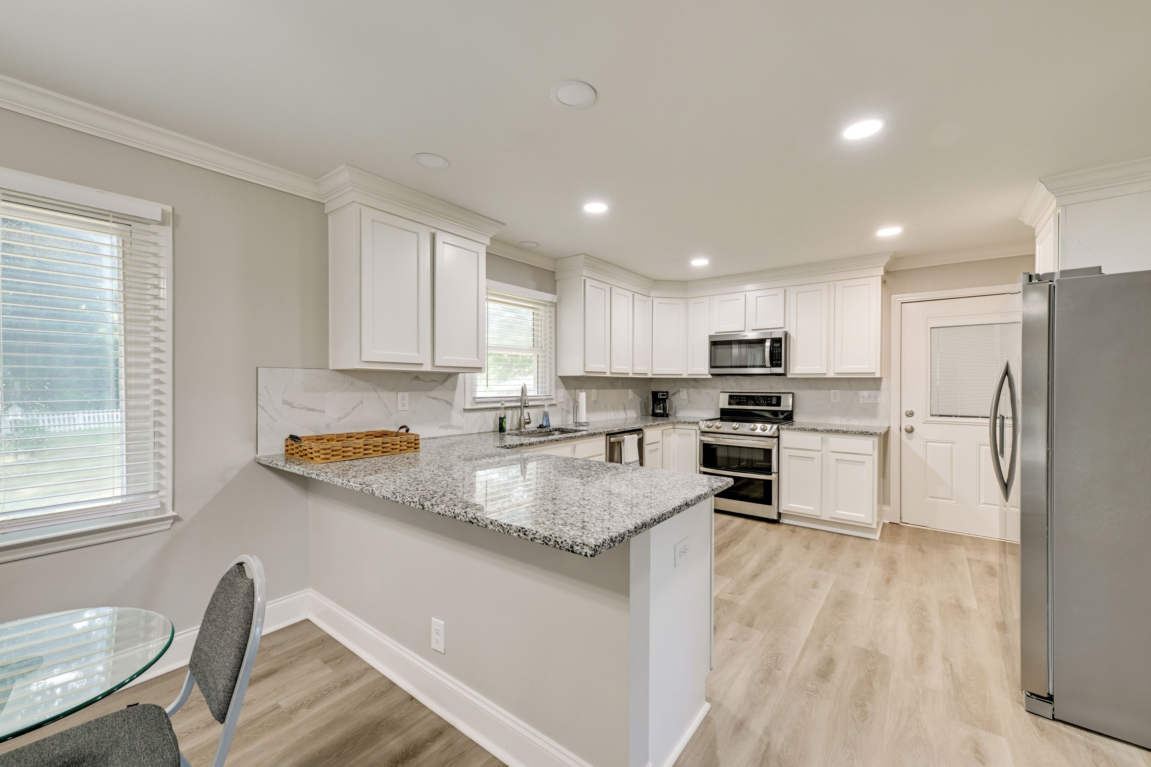 A modern kitchen with white cabinets, granite countertops, stainless steel appliances, and a glass dining table.