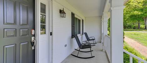 Eine Veranda mit geschlossener Tür, zwei Schaukelstühlen und einem kleinen Tisch.