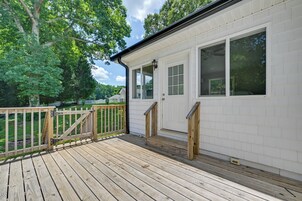 A wooden deck with a white building, a wooden fence, and trees in the background.