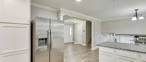 A modern kitchen with white cabinetry, a stainless steel refrigerator, and a granite countertop.