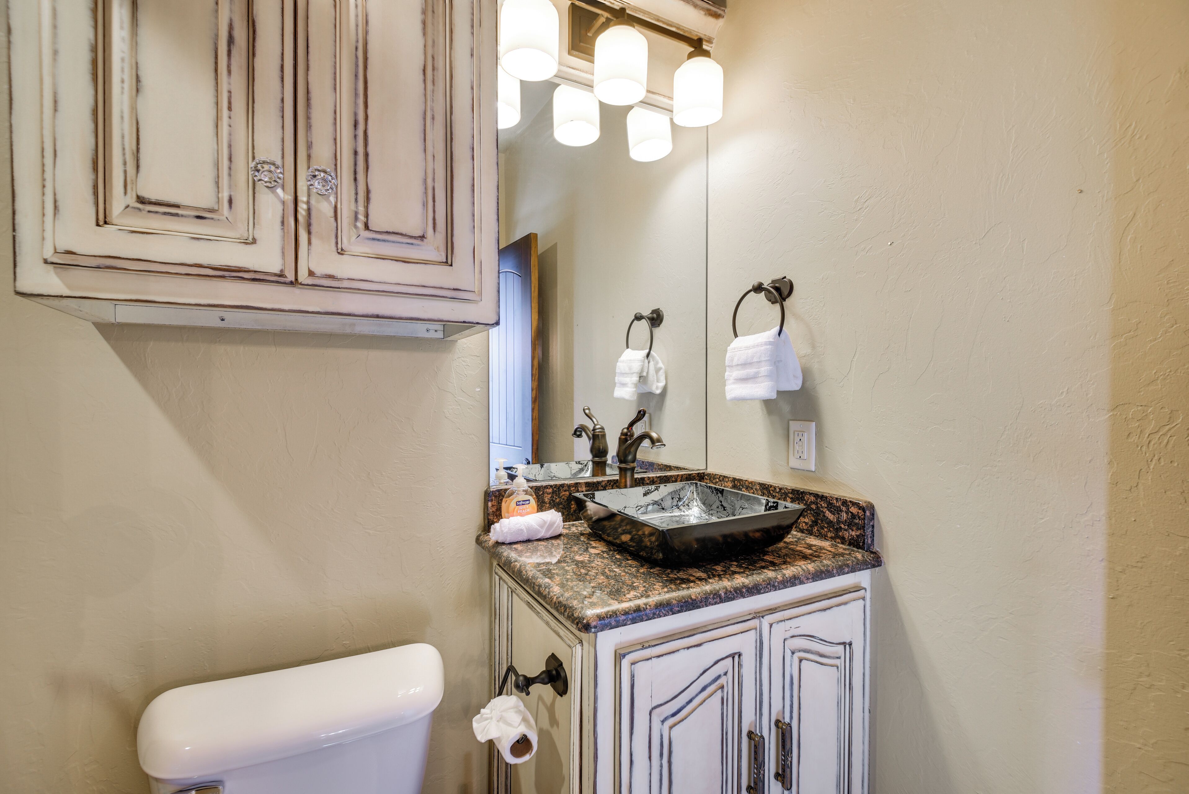 A bathroom with a white toilet, a sink with a granite countertop, and a mirror above the sink.