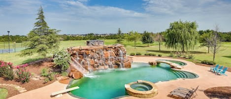 A backyard with a swimming pool, a hot tub, and a waterfall feature.