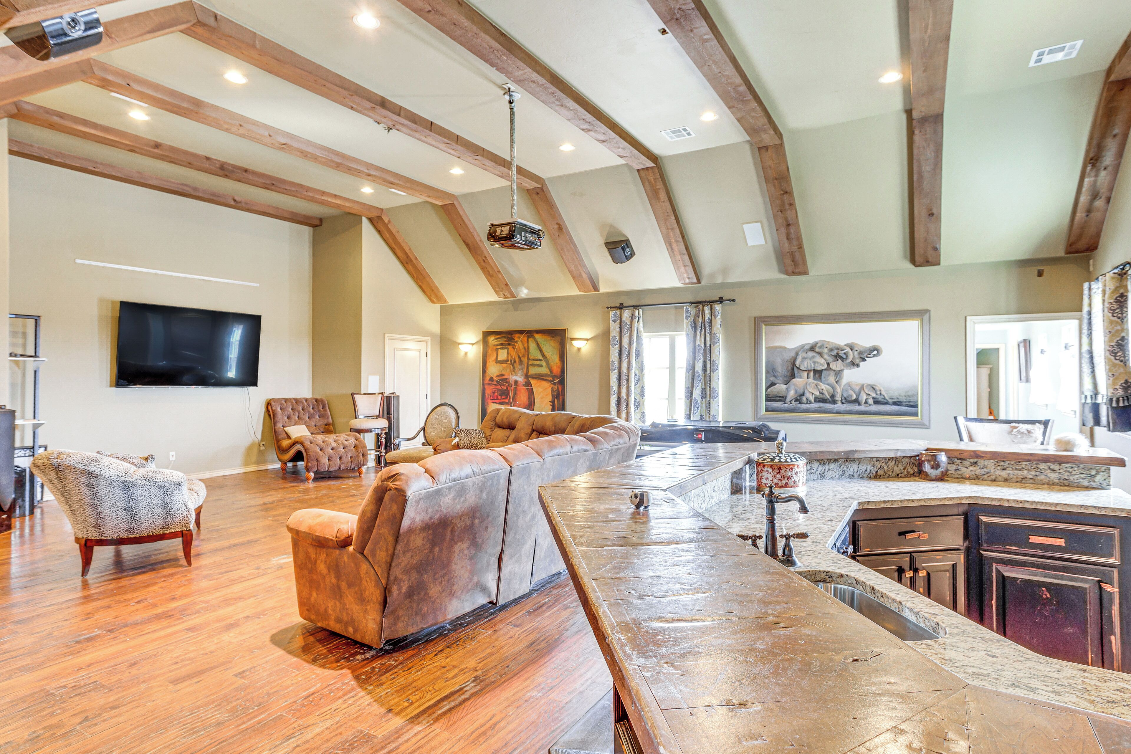 A spacious living area with a long wooden bench, a leather sofa, and a television mounted on the wall.