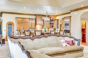 A spacious living room with a large beige sofa, wooden cabinets, and a chandelier.