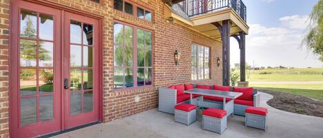 A covered patio with outdoor furniture, a brick building, and a balcony.