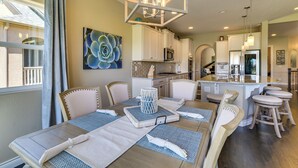 A dining area with a table set for six, a chandelier, and a kitchen in the background.