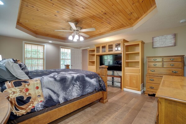 A bedroom with a bed, wooden ceiling, built-in TV, and wooden furniture.