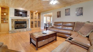 A living room with a stone fireplace, leather sofa, wooden shelves, and a ceiling fan.