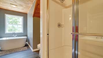 A bathroom with a freestanding bathtub, a glass-enclosed shower, and a window providing natural light.