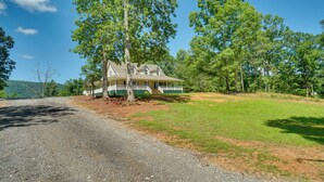 A house with a porch, surrounded by trees and a gravel driveway.
