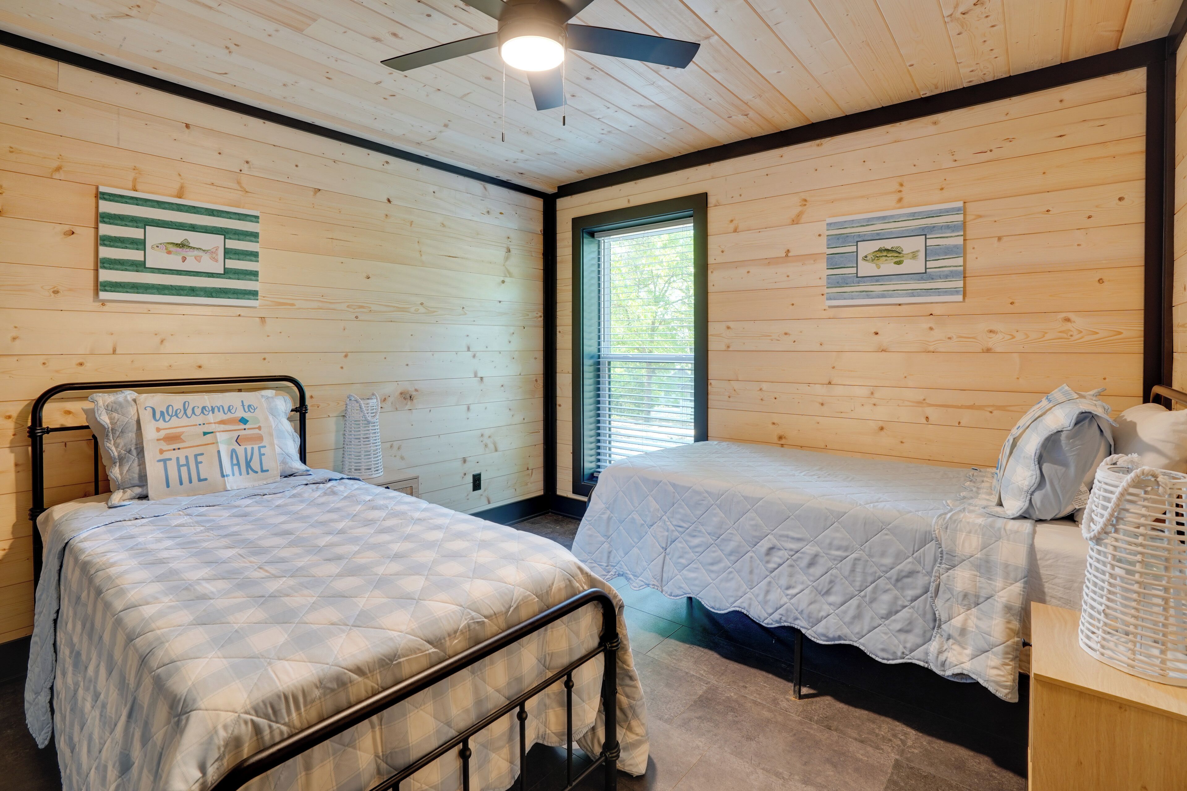 A room with two beds, a ceiling fan, wooden walls, and framed pictures.