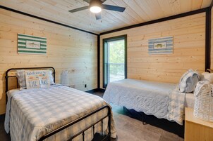 Una habitación con dos camas, ventilador de techo, paredes de madera y cuadros enmarcados.