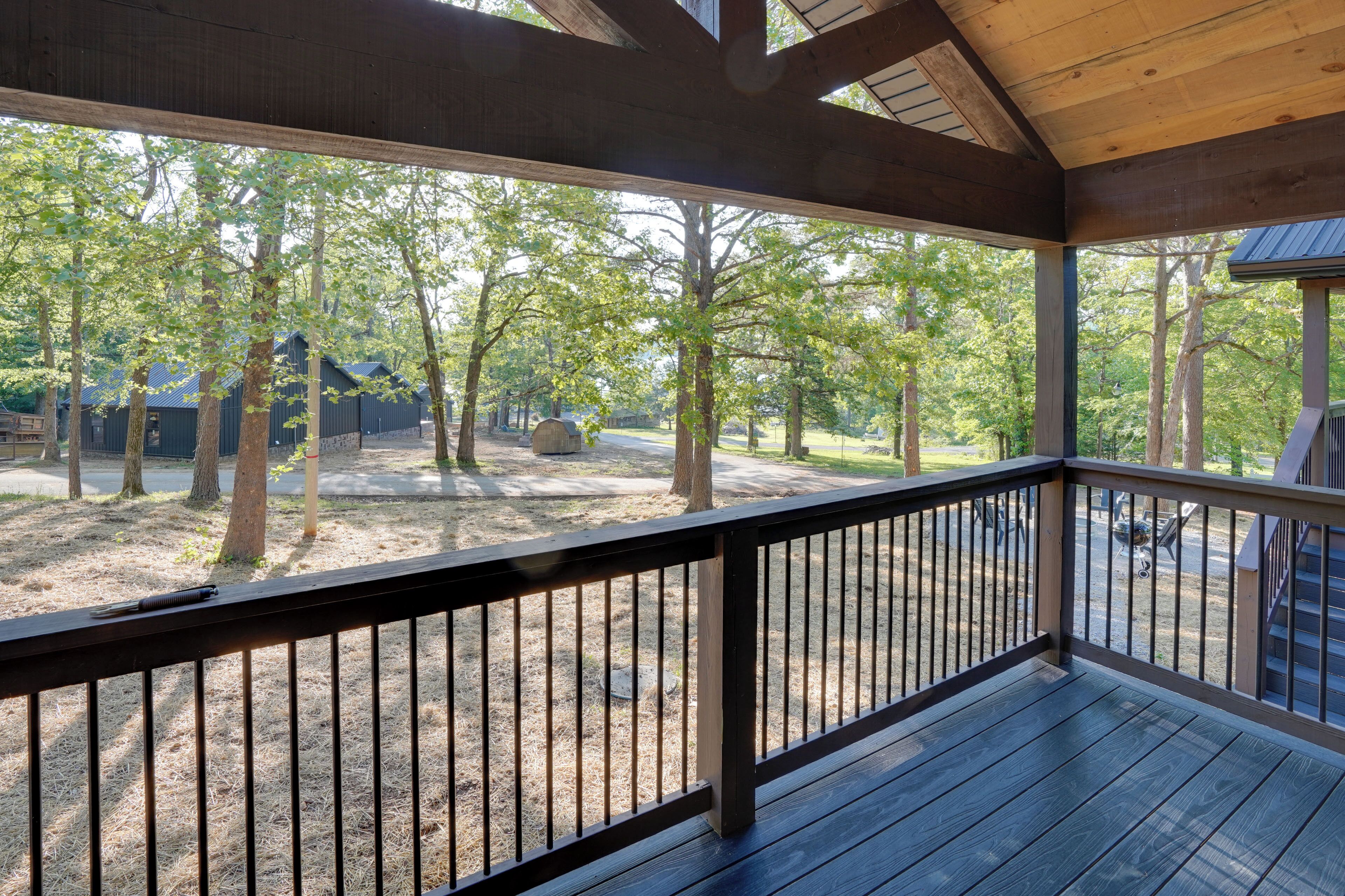 A covered outdoor area with a wooden deck and railing, surrounded by trees and a gravel path.
