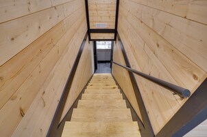Una escalera de madera con barandillas de metal que conduce a una habitación con ventana y rejilla de ventilación.