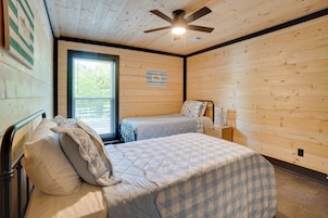 Dormitorio con dos camas, ventilador de techo, ventana y un interruptor de luz en la pared.