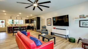A modern living room with a red sofa, a coffee table, a TV, and a ceiling fan. - 'the Romano Retreat' Modern Lake Guntersville Home (Scottsboro)