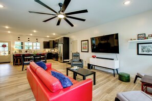 A modern living room with a red sofa, a coffee table, a TV, and a ceiling fan. - 'the Romano Retreat' Modern Lake Guntersville Home (Scottsboro)