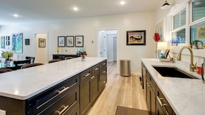 A modern kitchen with a central island, built-in appliances, and a dining area with chairs. - 'the Romano Retreat' Modern Lake Guntersville Home (Scottsboro)