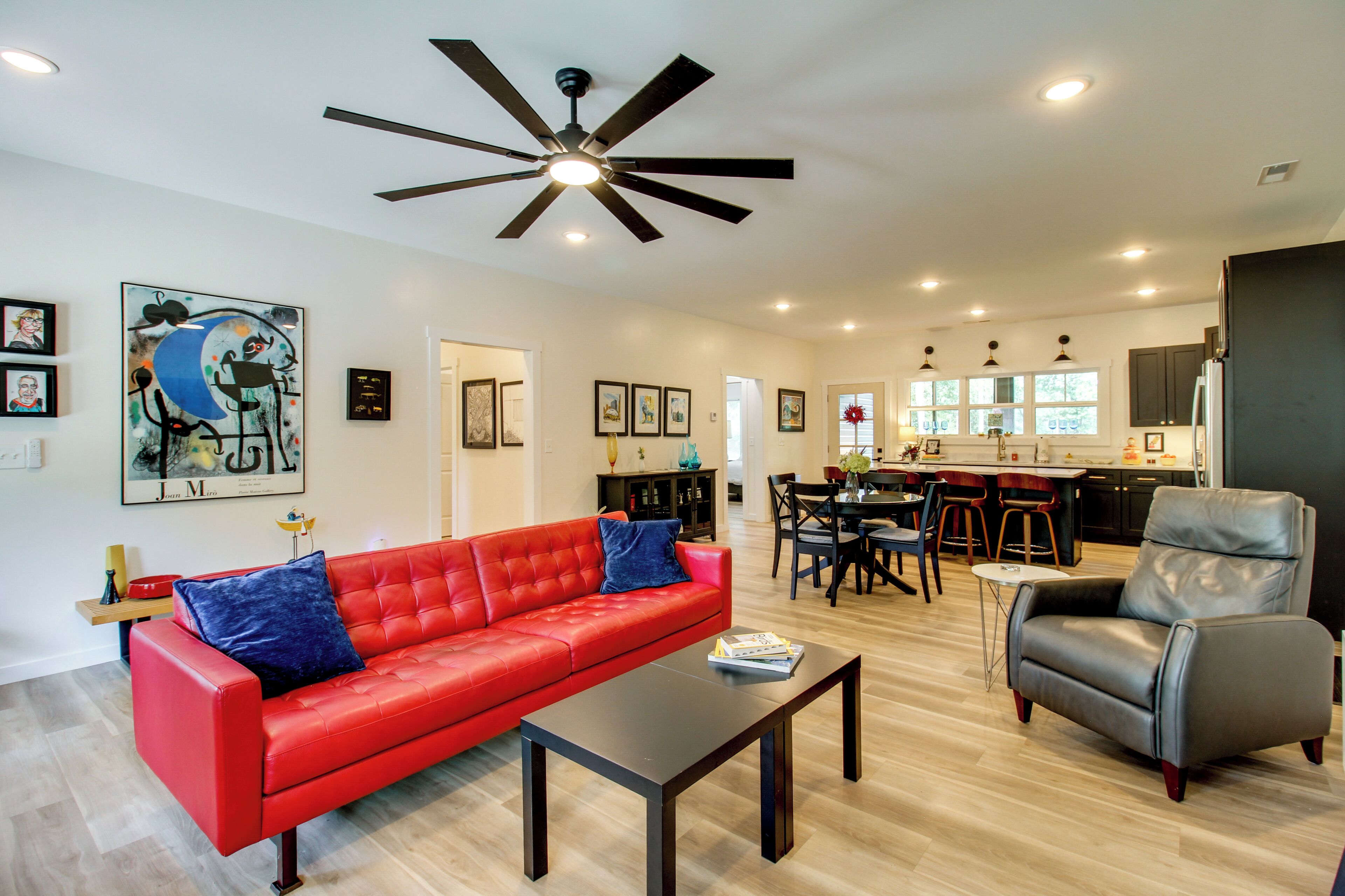 A spacious living area with a red sofa, a black coffee table, a grey armchair, and a ceiling fan.