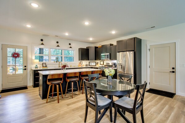 A modern kitchen with a central island, bar stools, stainless steel appliances, and a large window. - 'the Romano Retreat' Modern Lake Guntersville Home (Scottsboro)