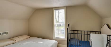 A bedroom with a bed, a crib, a window, and a radiator.