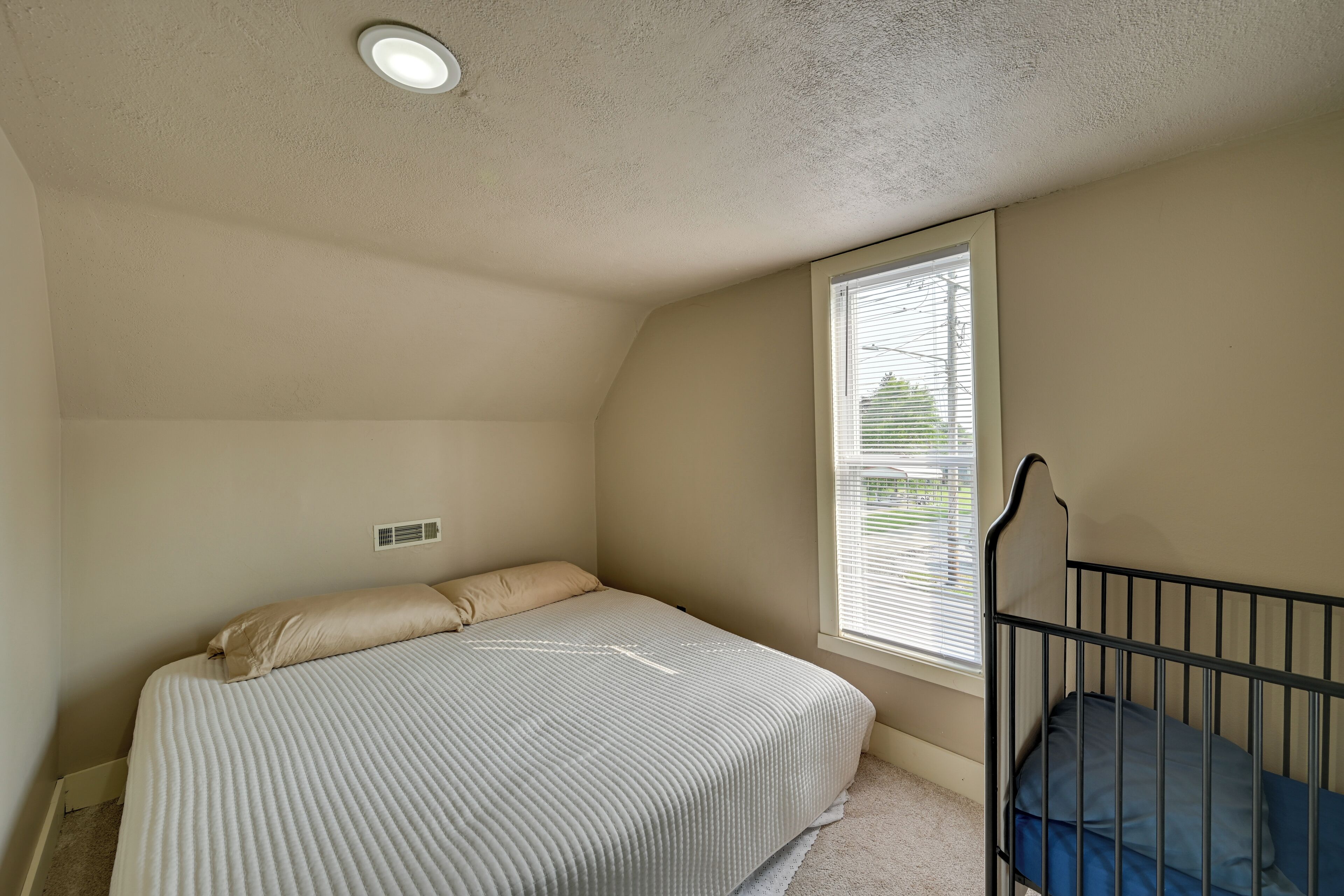 A bedroom with a bed, a window, and a crib.