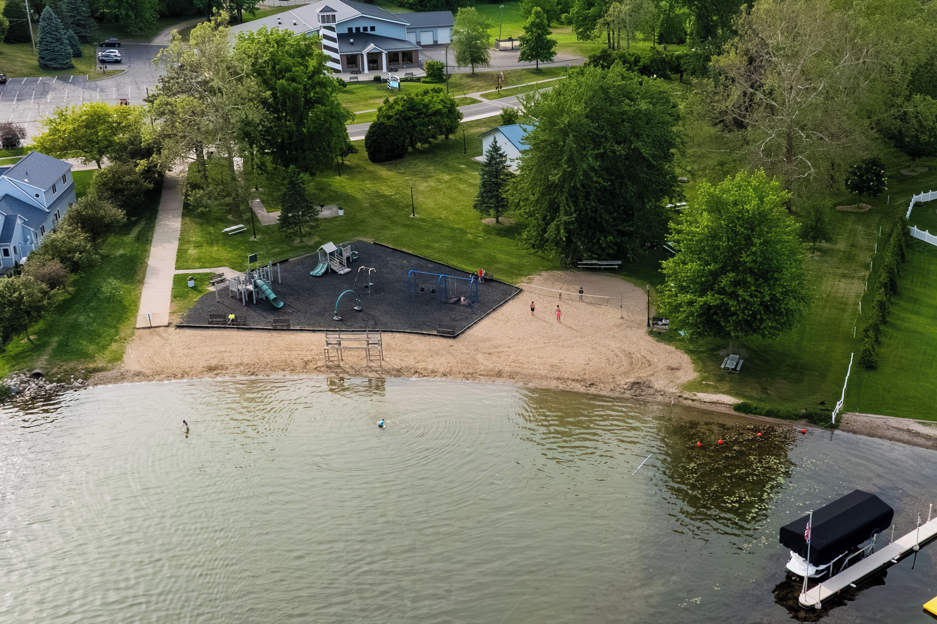 A lakeside park with a playground, a sandy area, and a boat dock.