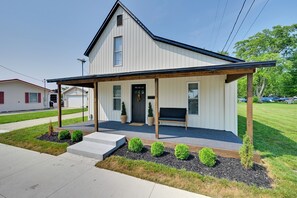 A two-story house with a covered porch, a front door, and a small front yard with shrubs.