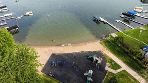 Un parque junto al lago con un área de juegos, una playa de arena y un puerto deportivo con barcos.