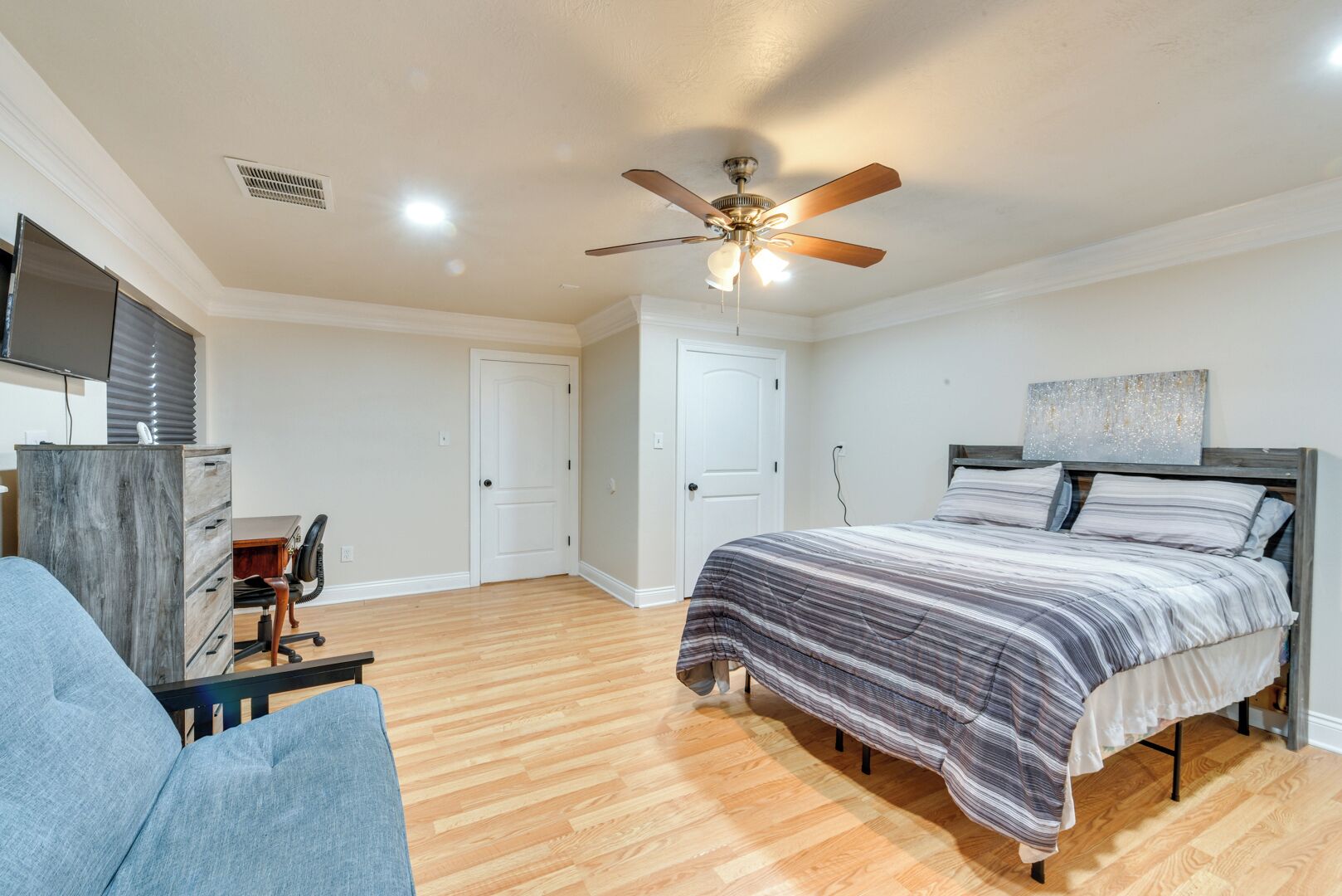 A bedroom with a bed, a desk, a chair, a ceiling fan, and a television.