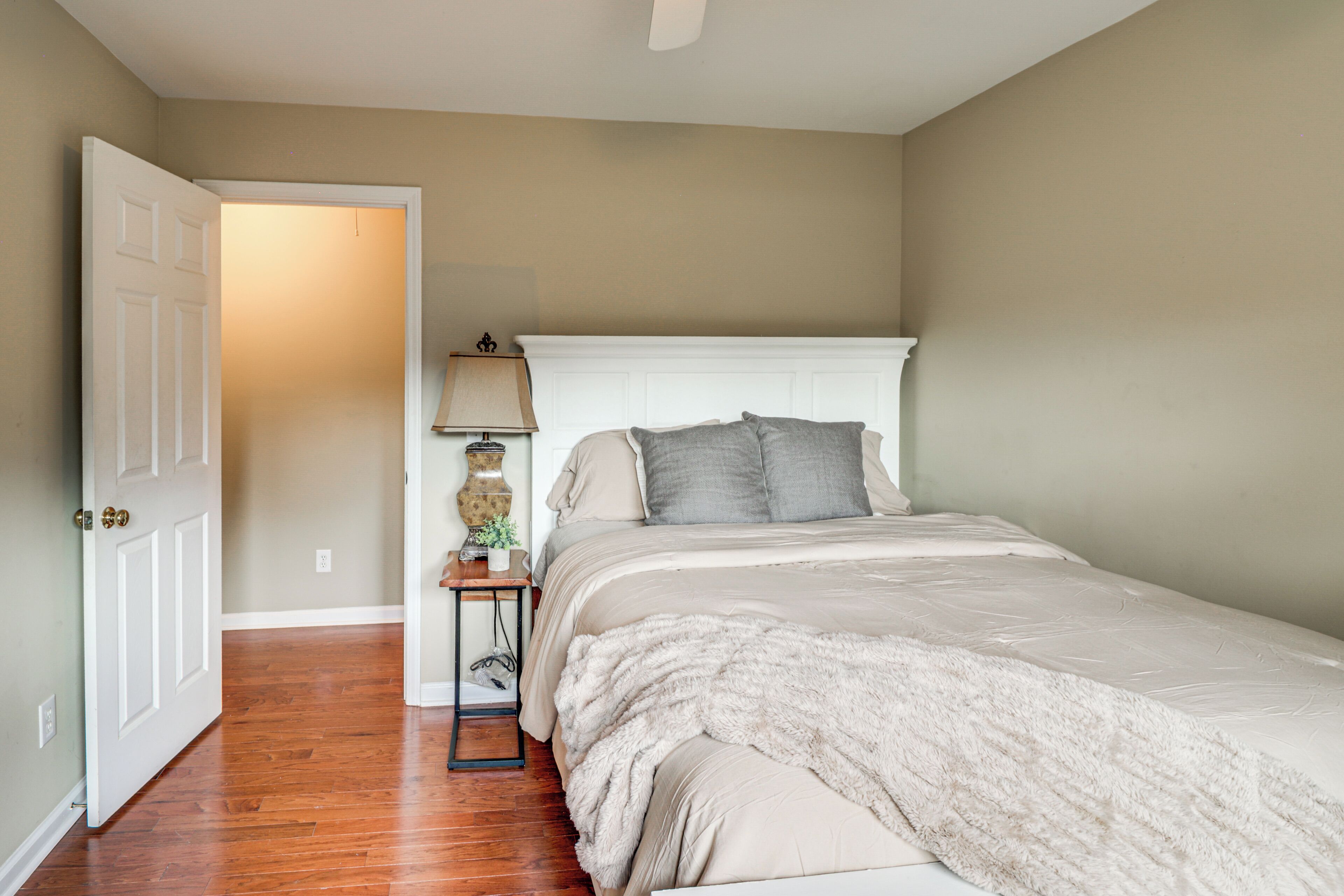 A bedroom with a bed, a nightstand, a lamp, and a door leading to another room.