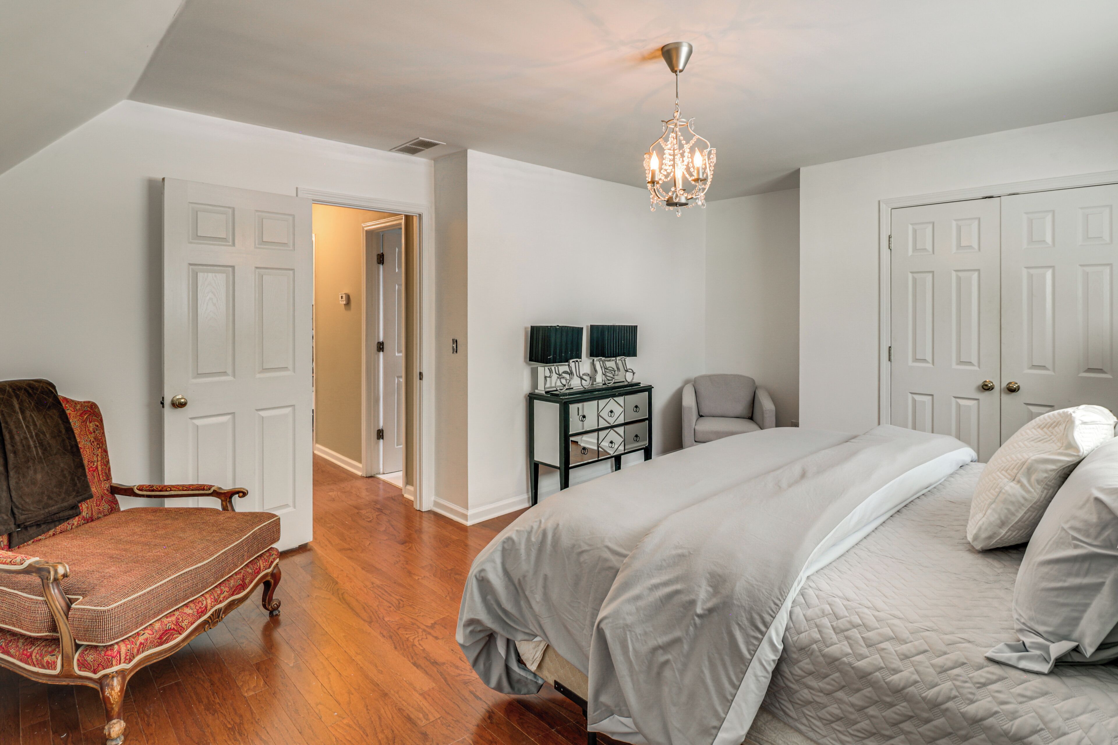 Een slaapkamer met een bed, een stoel, een dressoir en een kroonluchter.