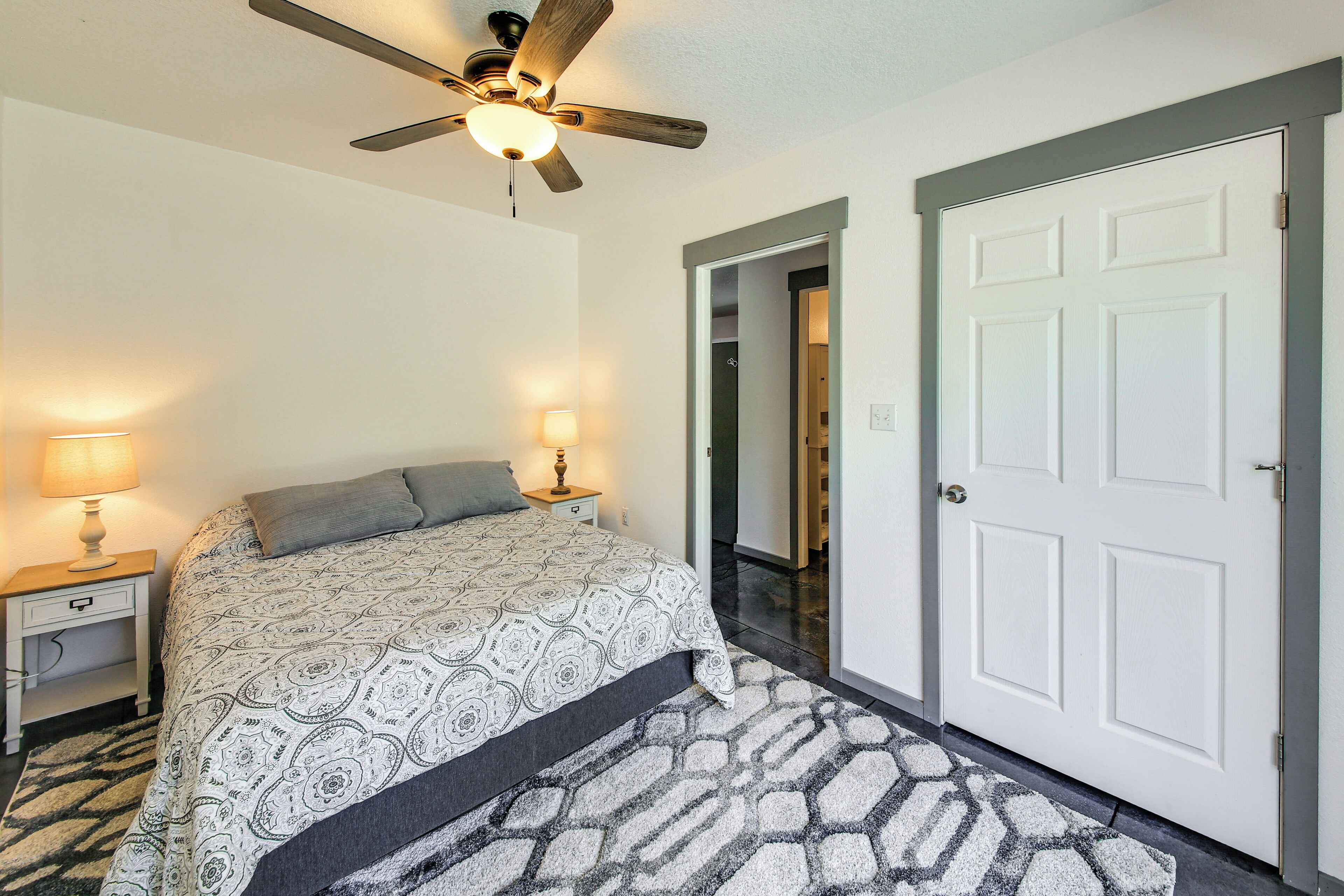 A bedroom with a bed, nightstands, a ceiling fan, a door, and a patterned rug.