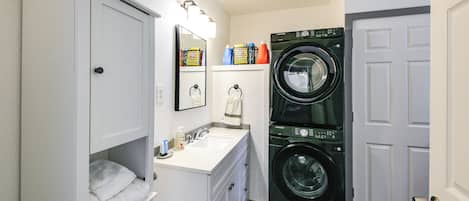 A compact laundry room with a washing machine, a sink, and a cabinet with folded towels.