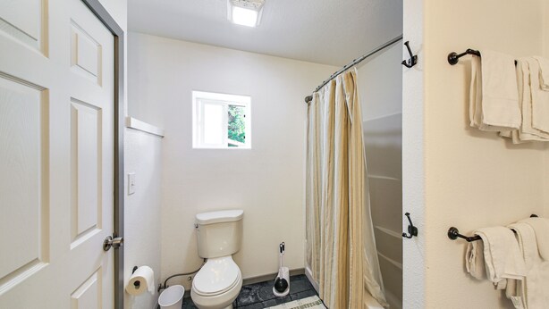 Een badkamer met toilet, een raam, douchegordijn en handdoeken op een rek.
