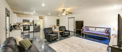 A modern living room with a sofa, two chairs, a coffee table, a fireplace, and a kitchen in the background.