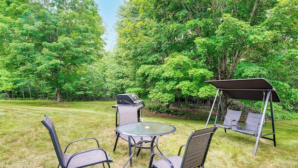 An outdoor seating area with a round table and chairs, a swing set, and a grill.
