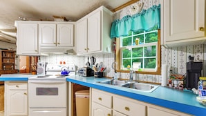 A kitchen with white cabinets, a blue countertop, a window with a view of greenery, and various kitchen appliances.