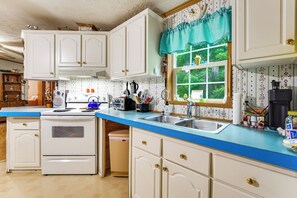 A kitchen with white cabinets, a blue countertop, a window with a view of greenery, and various kitchen appliances.