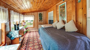 A wooden cabin room with a bed, a desk, and a window with curtains.