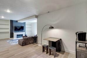 A modern living room with a flat-screen TV, a fireplace, a coffee table, and a desk with two chairs. - Quiet Tooele Retreat w/ Games + Fireplace (Tooele)