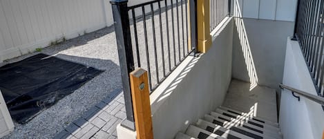 Un ensemble d’escaliers extérieurs avec une rambarde en métal noir, une main courante en bois et une clôture blanche en arrière-plan.