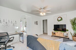 Una sala de estar moderna con un escritorio, un sofá, un televisor y un ventilador de techo.