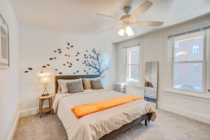 A bedroom with a bed, a ceiling fan, a nightstand, a lamp, a window, and a wall decoration. - Walk to Downtown! Central 2-apt Combo in Pottstown (Pottstown)